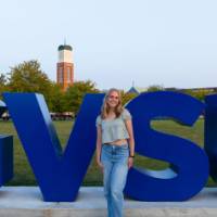 Woman standing in front of GVSU lettering on Kirkhof Lawn, smiling